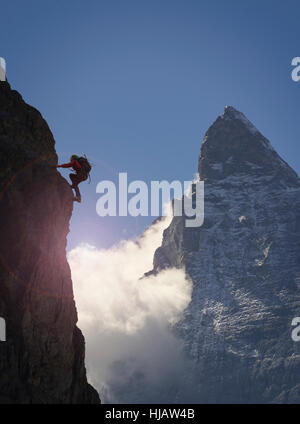 Silhouetted female climber climbing rock face near Matterhorn, Canton Wallis, Switzerland Stock Photo