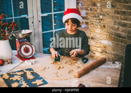 Boy in Santa hat preparing Christmas cookies at kitchen counter Stock Photo