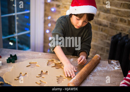 Boy in Santa hat preparing Christmas cookies at kitchen counter Stock Photo