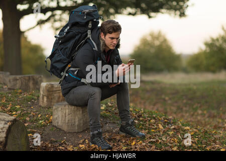 Young man sitting on tree stump, using smartphone Stock Photo