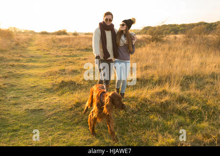 Young couple walking dog in field Stock Photo
