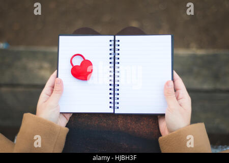 female Hands holding notebook with closed red padlock in heart shape Stock Photo