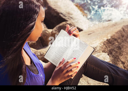 Young girl reading her Bible by the sea Stock Photo