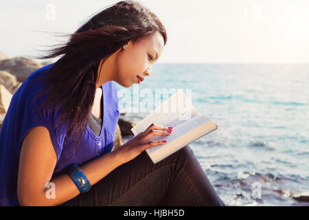 Beautiful Girl reading her Bible by the sea Stock Photo