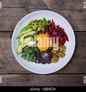 Nourish Bowl with Edamame, Black Rice, Avocado, Spinach, kale, carrot, cashews and beetroot on a Rustic wood background Stock Photo