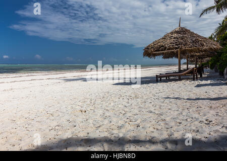 Sandy beach with wooden sun shades with straw roof and sun beds, blue sky, hotel resort, sunny day in October, Zanzibar,Tanzania, Africa Stock Photo