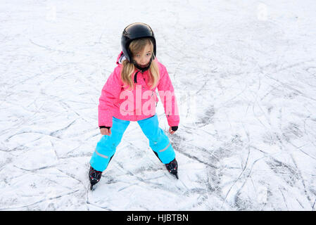 Happy little girl skating in winter outdoors, wearing safety helmet Stock Photo