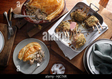 Bistro table with herb crusted lamb racks and rustic chicken pie Stock Photo