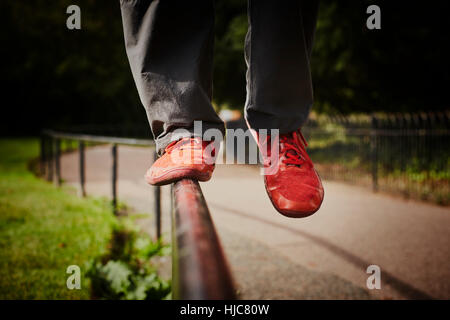Man training in park, legs and red trainers balancing on fence Stock Photo