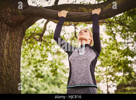 Young woman doing pull ups on park tree branch Stock Photo