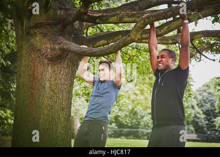 Personal trainer and young man doing pull ups using park tree branch Stock Photo