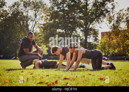 Personal trainer instructing man and women doing push ups in park Stock Photo