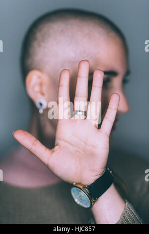 Portrait of young woman with shaved head and hand in front of face Stock Photo