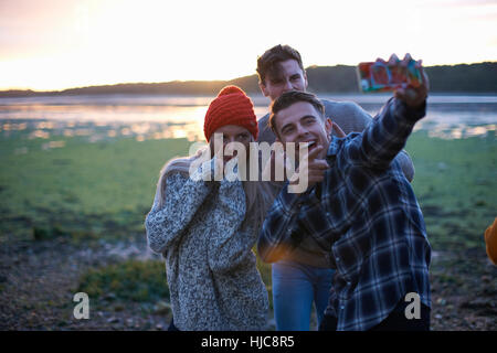 Three young adults taking smartphone selfie at seaside sunset Stock Photo