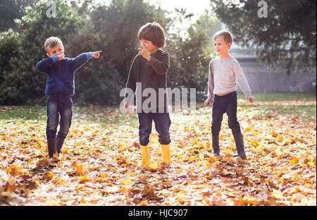 Three boys playing outdoors, in autumn leaves Stock Photo