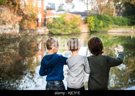 Three young boys, standing beside lake, rear view Stock Photo