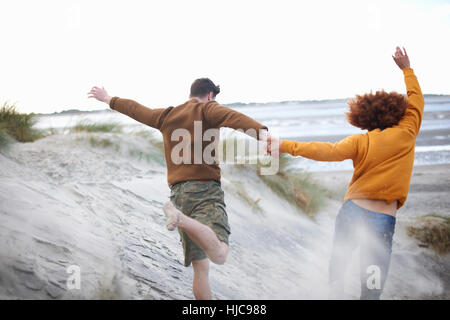 Couple running down sand dunes to beach Stock Photo