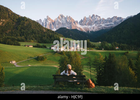 Woman relaxing on park bench, Santa Maddalena, Dolomite Alps, Val di Funes (Funes Valley), South Tyrol, Italy Stock Photo