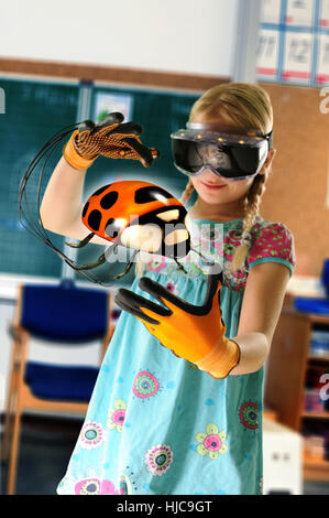 Girl pretending to be teacher wearing virtual reality headset and gloves to show ladybird Stock Photo