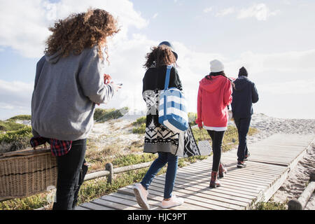 Rear view of young adult friends strolling along beach boardwalk reading smartphones, Western Cape, South Africa Stock Photo
