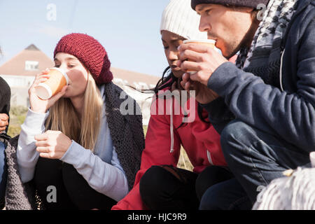 Young adult friends crouching on beach drinking takeaway coffee, Western Cape, South Africa Stock Photo