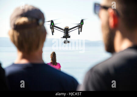 Rear view of man and woman looking at drone flying mid air over coast, Split, Dalmatia, Croatia Stock Photo