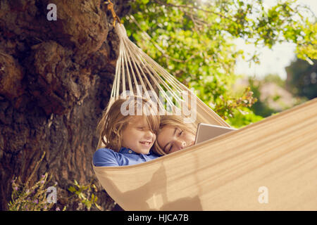 Teenage boy and brother reclining in garden hammock browsing digital tablet Stock Photo