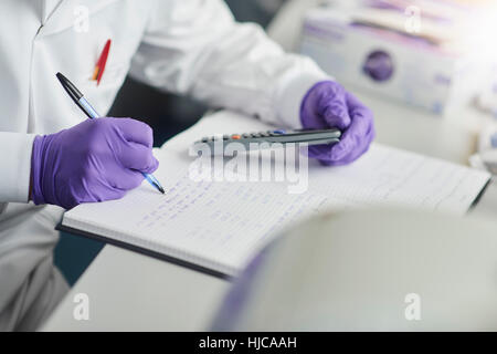 Scientist using calculator writing in notebook Stock Photo
