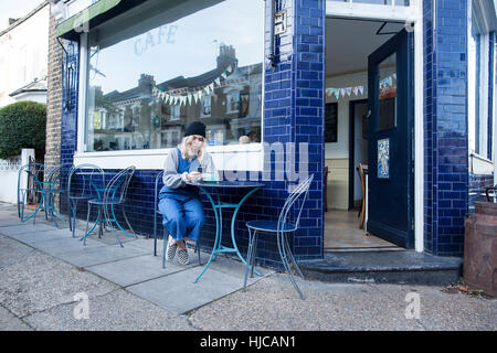 Young woman sitting outside cafe, using smartphone Stock Photo