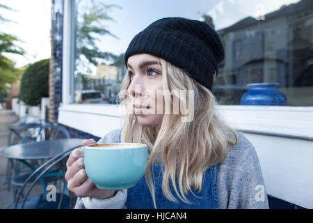 Young woman sitting outside cafe, drinking cup of tea Stock Photo