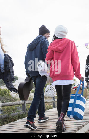 Rear view of young adult picnicking friends strolling along boardwalk at beach, Western Cape, South Africa Stock Photo