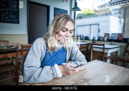 Young woman sitting in cafe, using smartphone, smiling Stock Photo