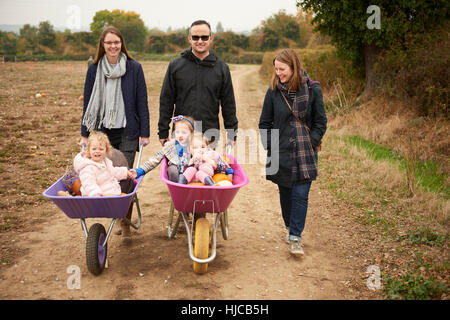 Portrait of parents pushing three girls in wheelbarrows along pumpkin field Stock Photo