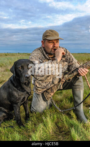 A wildfowler, or duck hunter, with his dog on the Lincolnshire marsh blowing into a duck call Stock Photo