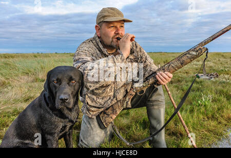 A wildfowler, or duck hunter, with his dog on the Lincolnshire marsh blowing into a duck call Stock Photo