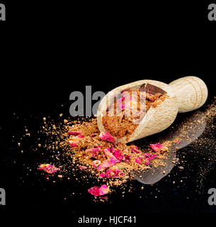 Ras el hanout, luxury spice mix with rose petals. Typical of Morocco, north Africa. With scoop on shiny black background. Stock Photo