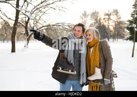 Senior couple in winter nature with ice skates going to rink.