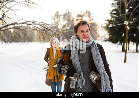 Senior couple in winter nature with ice skates going to rink.