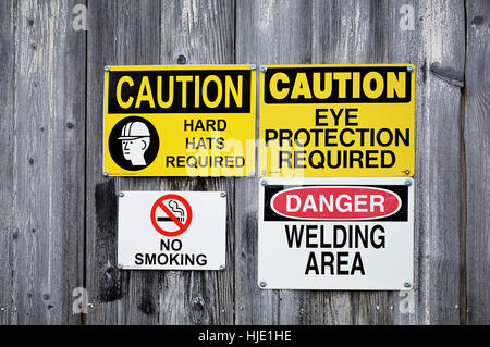 A group of hard hat, eye protection,welding area, and no smoking signs on a wood wall. Stock Photo