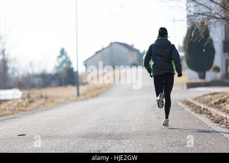 rear view of a woman running in the streets of a little town during winter or autumn Stock Photo