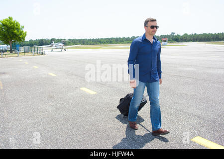 Man walking at airport pulling suitcase Stock Photo