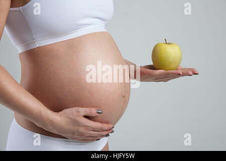 Belly of a pregnant woman with green apple on her hand Stock Photo