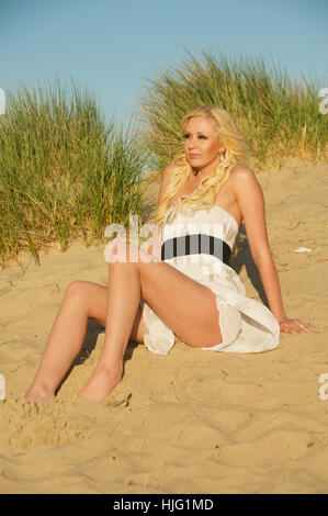 Beautiful long haired blonde young woman in a summer dress on the beach. Stock Photo
