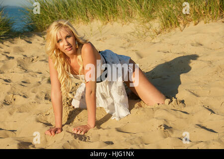 Beautiful long haired blonde young woman in a summer dress on the beach. Stock Photo