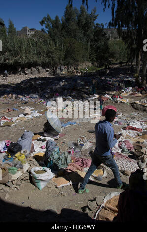 Man walking through a market in Ethiopia, littered with rubbish, an older woman selling spices and one under an umbrella Stock Photo