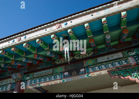 Close up of hand painted wooden eaves and beams with colorful geometric and floral patterns on Buddhist temple roof with icicles Stock Photo