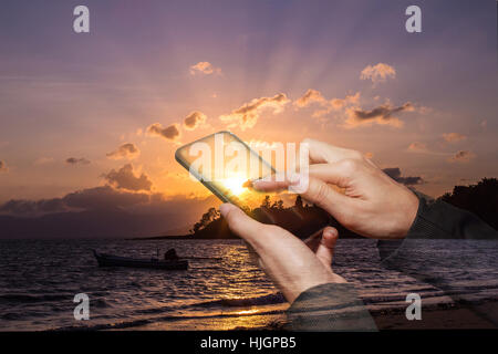 double exposure of woman hand touch screen smart phone over sunrise on the beach Stock Photo