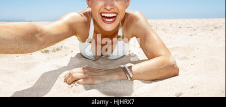 Heading to white sand blue sea paradise. Smiling woman in white swimsuit and funky glasses taking selfies while laying on sandy beach on a sunny day Stock Photo