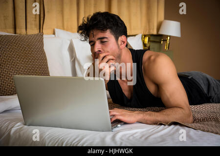 Young Man Doing Homework on Laptop in Bedroom Stock Photo