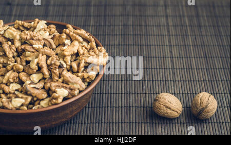 Walnut kernels and whole walnuts in brown ceramic bowl. Healthy organic food concept. Selective focus Stock Photo